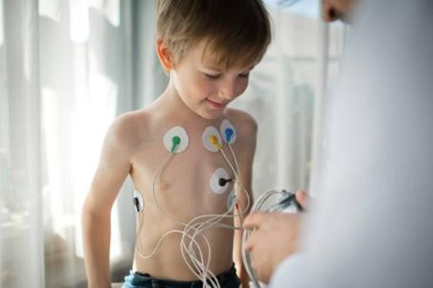 Young boy standing shirtless as a clinician attaches ECG electrodes to his chest for monitoring.