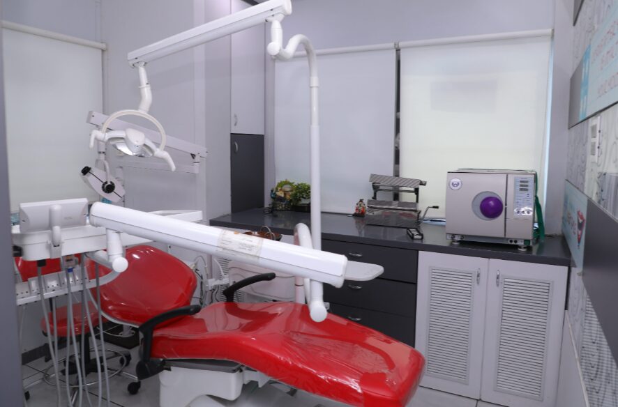 Dental treatment room with a red dental chair, overhead light, and attached equipment.