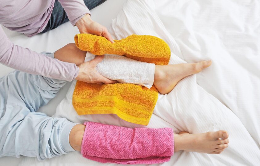 p3 - Sparsh Hospital Caregiver supporting a child's leg with a white wrap while colorful towels rest on a white bed.