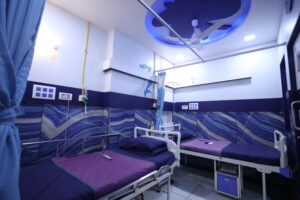 2 - Sparsh Hospital Hospital ward with blue dolphin mural, multiple beds with purple sheets and blue pillows, curtains, and medical equipment along the walls.