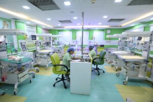4 - Sparsh Hospital Neonatal intensive care room with multiple incubators, monitors, and two nurses in green scrubs attending work stations.