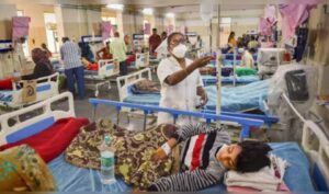 Picture1 - Sparsh Hospital Crowded hospital ward with several patients in beds; a nurse in a mask tends to a patient in the foreground.