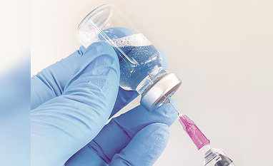Healthcare worker wearing blue gloves draws liquid from a vial with a syringe ready to inject.
