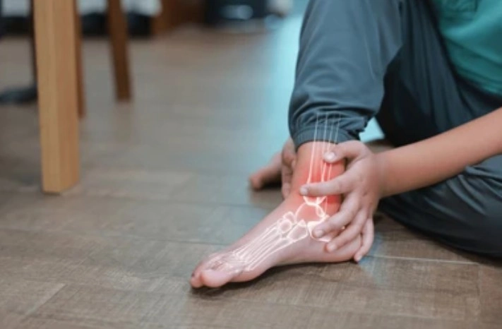 Person sits on the floor holding their ankle, with a glowing outline of the foot bones highlighting pain or injury location.