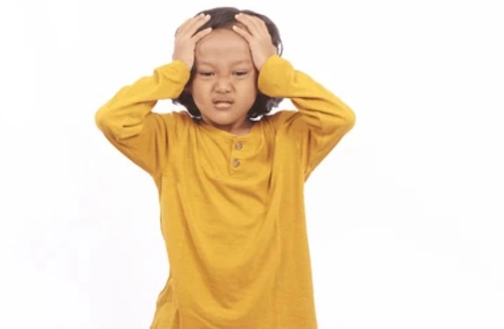 Chronic Medical Conditions - Sparsh Hospital - Sparsh Hospital Young child in a yellow shirt holds their head with a frustrated expression against a white background.