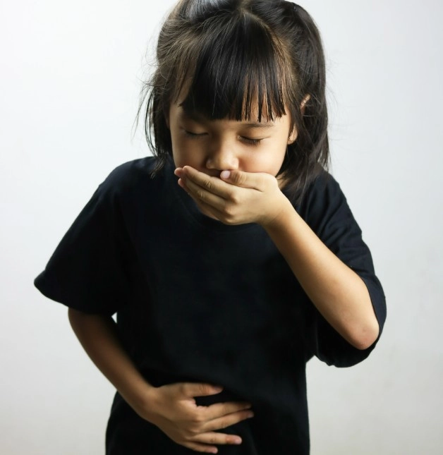Dehydration Due to Vomiting or Diarrhoea - Sparsh Hospital - Sparsh Hospital Young girl in a black shirt covering her mouth with one hand and holding her stomach, appearing nauseous.