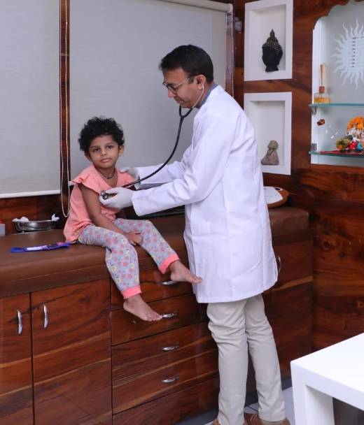 In Patient Care - Sparsh Hospital - Sparsh Hospital Pediatrician checks a young girl's heartbeat with a stethoscope during a clinic visit on a wooden counter.