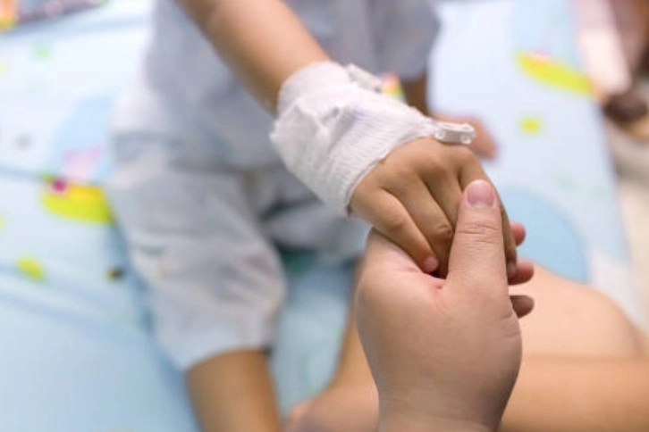 Post-Surgical Monitoring - Sparsh Hospital - Sparsh Hospital Adult gently holds a child's bandaged hand, offering support in a medical setting.