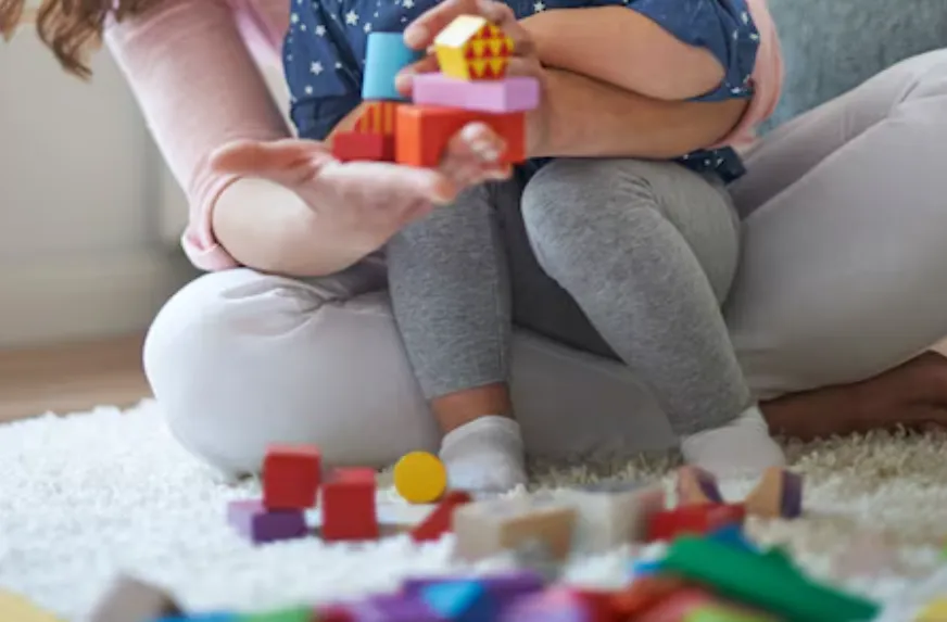 Parent and child sitting on a rug, stacking colorful toy blocks together.