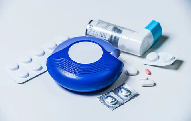 What Treatment Options Are Available for Asthma in Children - Sparsh Hospital - Sparsh Hospital Blue inhaler spacer (aerobi spacer) with an inhaler and assorted pills on a white surface, illustrating asthma/COPD medication tools, ready for use or storage.