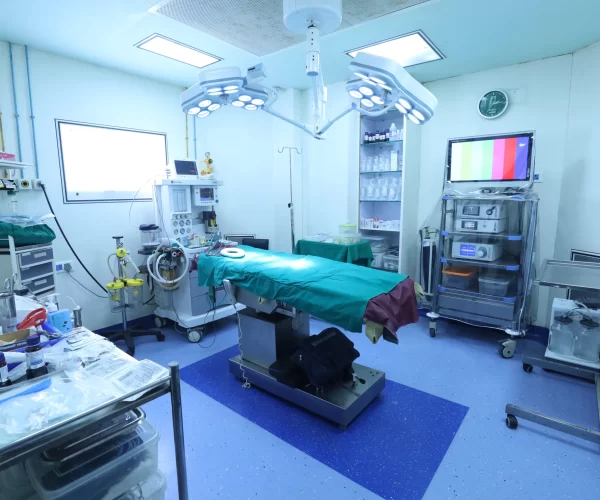 Bright surgical operating room with overhead lamps, patient table, and medical equipment ready for surgery